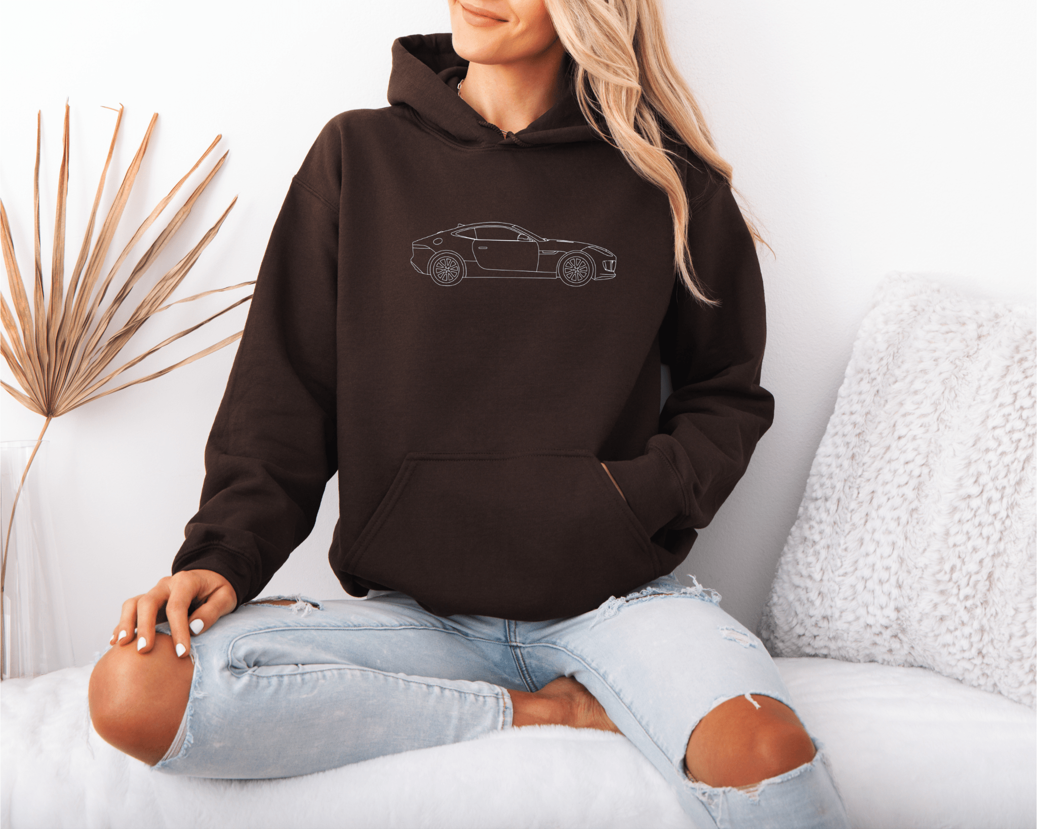 Person wearing a brown hoodie with a car design, sitting on a white couch.