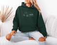 Load image into Gallery viewer, Person wearing a dark green hoodie with a car design, sitting on a white couch.
