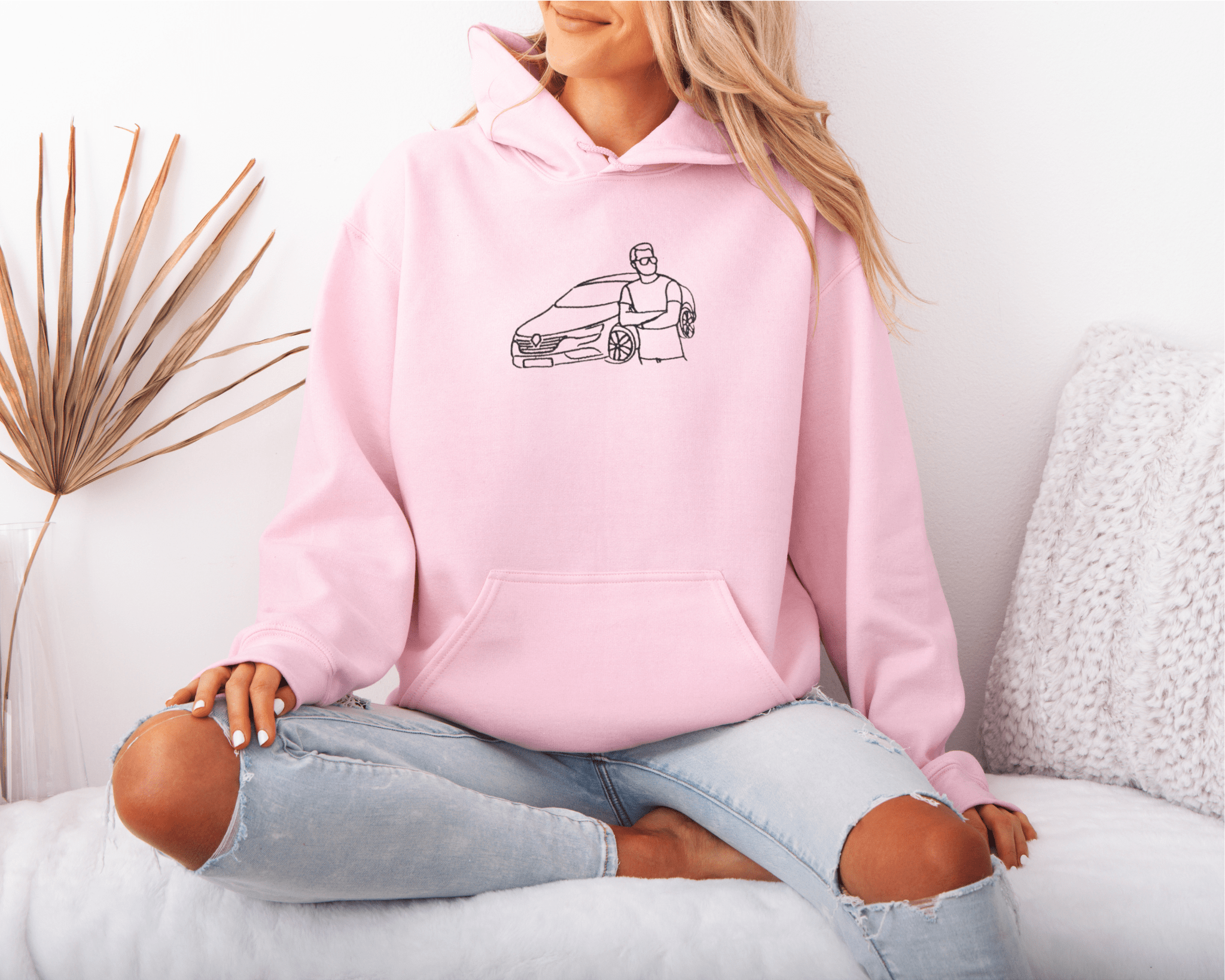 Person wearing a pink hoodie with a car embroidered design sitting on a couch.